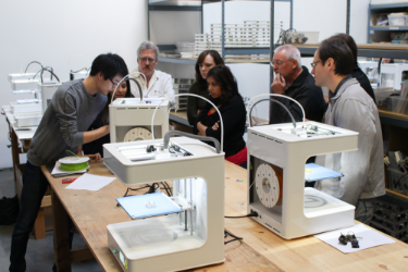 Teachers closely observing teachers using several 3D printers.